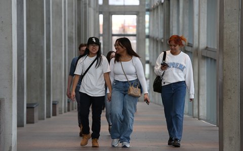 A wide shot of three young individuals smiling and walking up a long hallway.