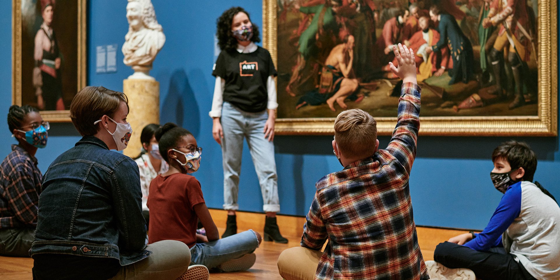Students sitting on the ground in front of artworks.